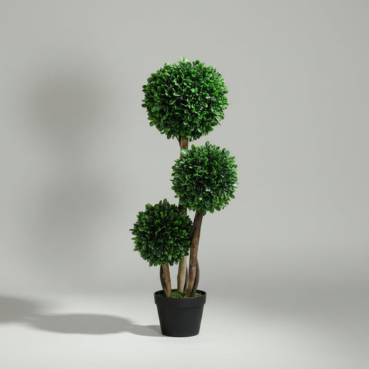 Decorative indoor plant in a pot on a wooden floor with a side table and boots in the background.